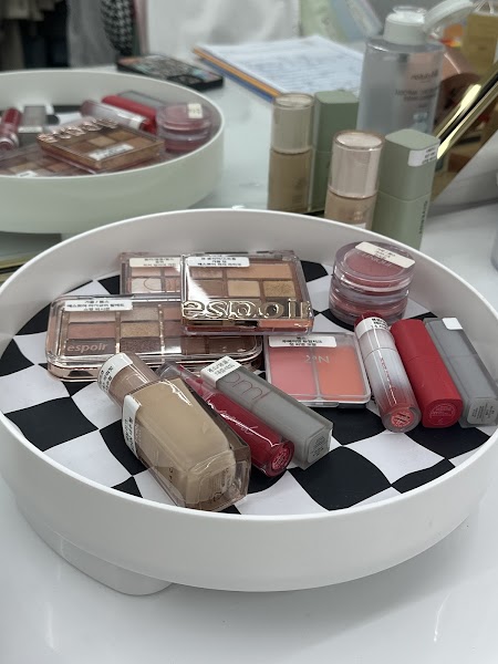 A white circular turntable tray filled with various cosmetic palettes, lipsticks, and foundations on a white desk