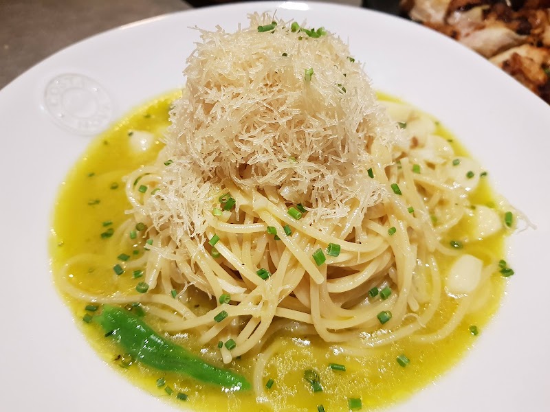 A plate of spaghetti with shaved cheese garlic and chives in a savory sauce