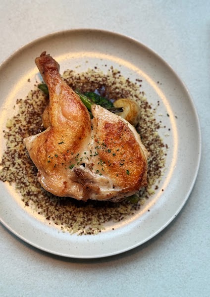 Roasted chicken served over a bed of grains and vegetables on a neutral plate.