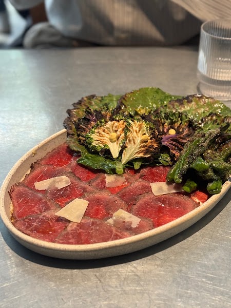 Beef carpaccio with charred greens and shaved cheese on brushed steel tabletop