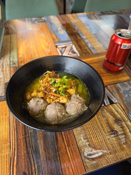 A bowl of Indonesian meatball soup known as bakso served on a rustic wooden-style table