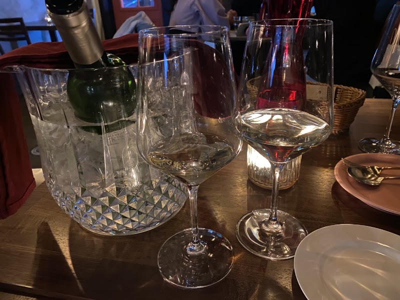 Wine bottle in an ice bucket and filled wine glasses on a restaurant table.