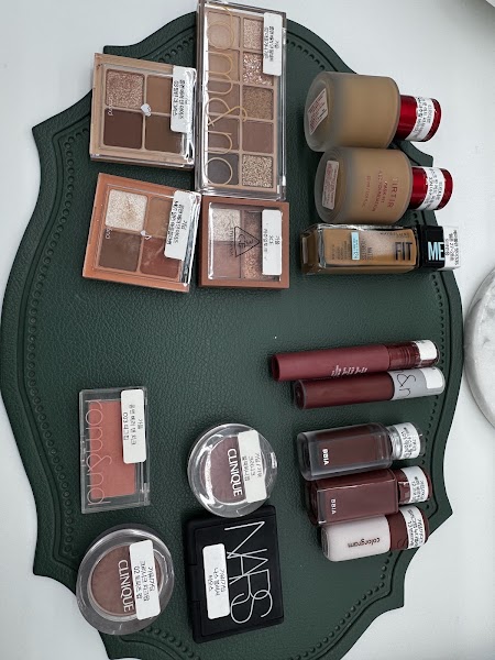 Collection of various cosmetics including eyeshadow palettes, foundations, and lip products on a green mat