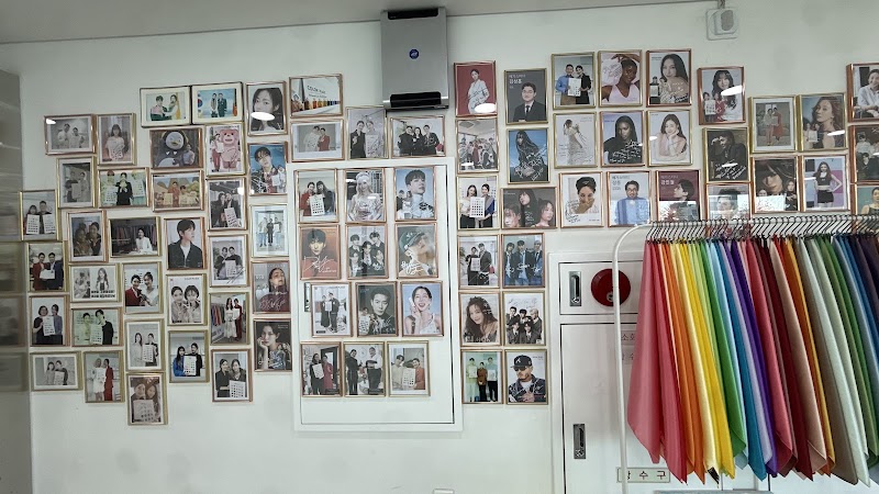 Studio display wall with client photo portraits and a rack of rainbow-spectrum fabric draping swatches