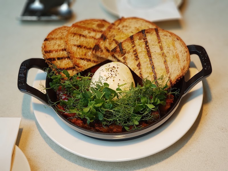 A gourmet brunch dish featuring grilled bread, poached egg, and fresh herbs in a black cast-iron skillet.