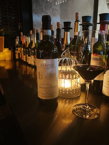 A wine glass and a bottle of Barolo wine displayed on a dimly lit restaurant counter with a decorative candle lantern