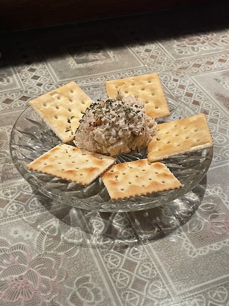 A scoop of spread topped with herbs served with square crackers on a decorative glass plate.