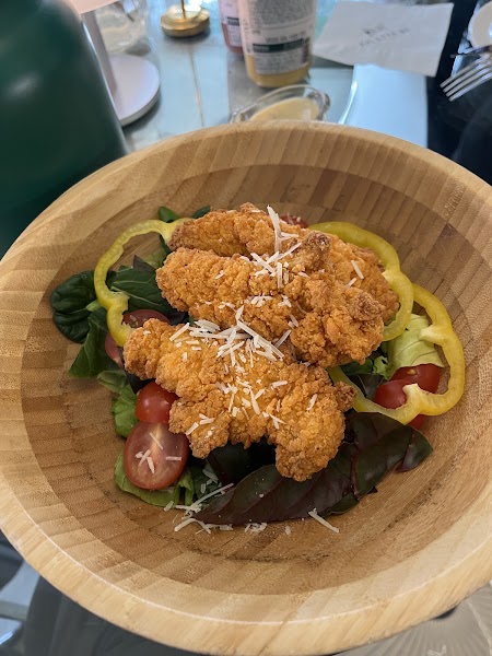 Crispy golden chicken tenders served in a wooden bowl over fresh salad greens with cherry tomatoes and bell peppers