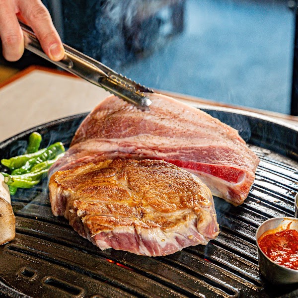 Thick pork shoulder butt seared to golden-brown crust with green chilies on cast iron pan
