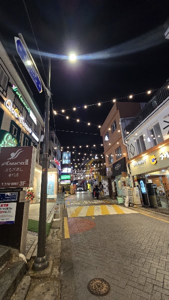 Street scene in Myeongdong, Seoul at night with string lights, storefront signs, and a marked crosswalk