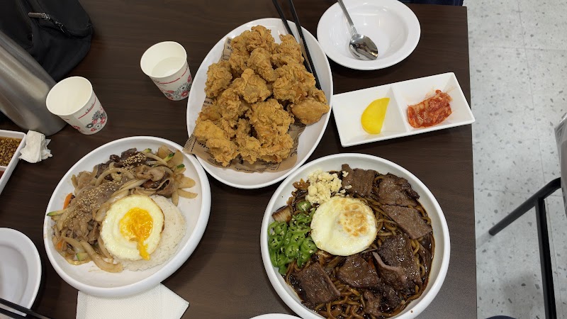 Top-down view of fried chicken, a rice bowl with egg, and noodles with beef and egg at a restaurant table.