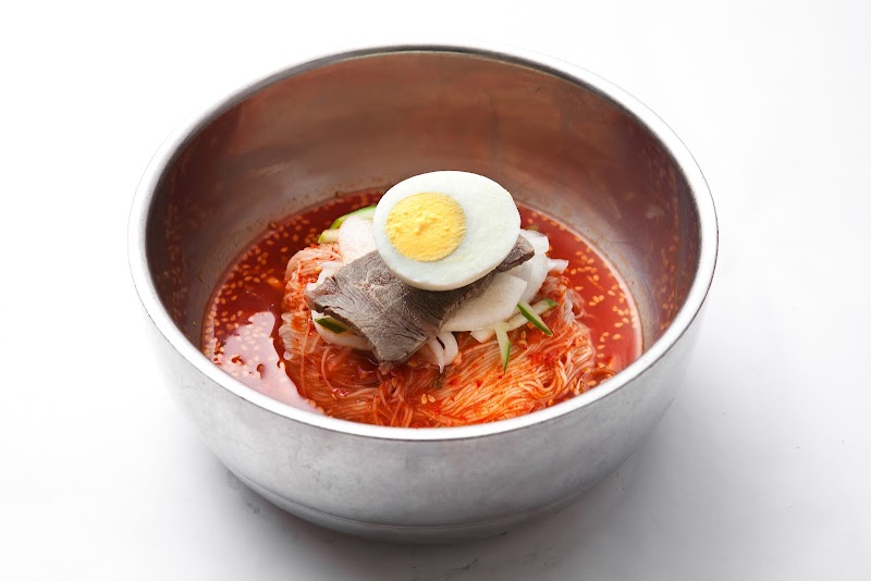A bowl of spicy Korean cold noodles topped with sliced beef and half a boiled egg.