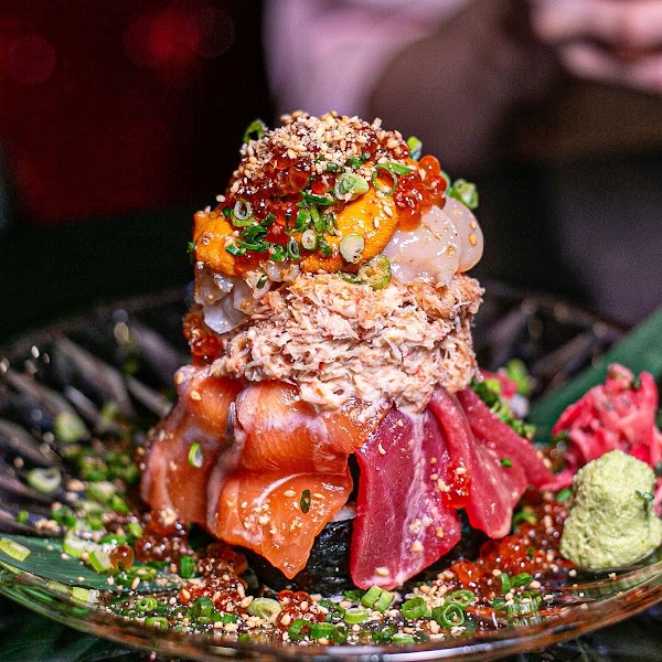 A tower of assorted sashimi including salmon, tuna, crab meat, uni, and salmon roe served on a glass plate.