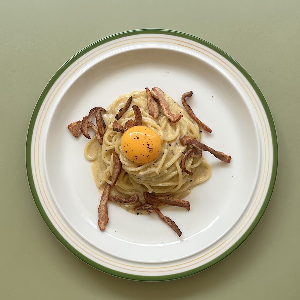 Signature pasta carbonara topped with fresh egg yolk and crispy bacon on a classic white and green rimmed plate