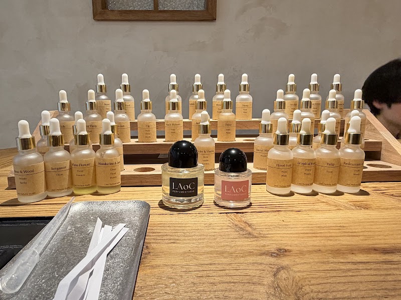 Many small frosted glass perfume bottles with dropper caps arranged on a tiered wooden display stand.