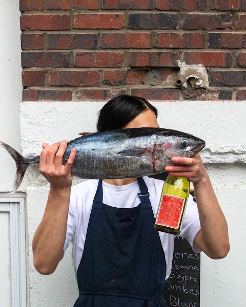 Bistro team member holding a whole fresh fish and bottle of wine in apron