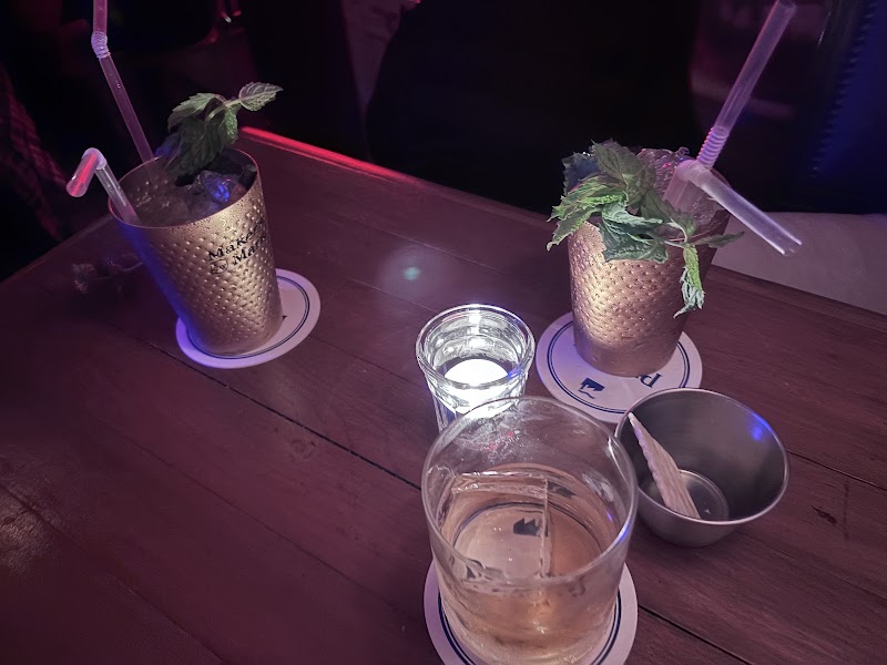 Two textured copper mugs and whiskey glass on a wooden table at the bar
