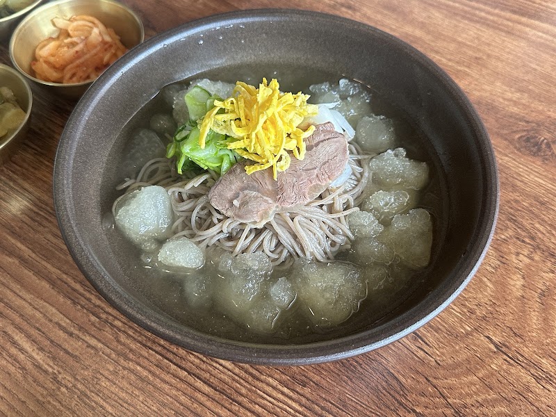Cold buckwheat noodles served in a dark ceramic bowl with beef and egg garnish over crushed ice