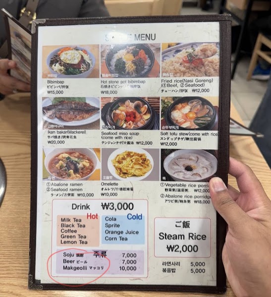 A handheld menu at Busan Jib restaurant in Seoul displaying various Korean food and drink options with prices