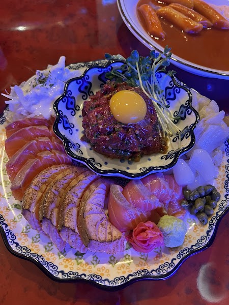 Platter of raw beef tartare, salmon sashimi, and seared salmon served on a decorative plate.