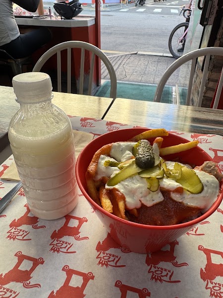 A bowl of fries topped with meat, sauce, and pickles on a paper liner