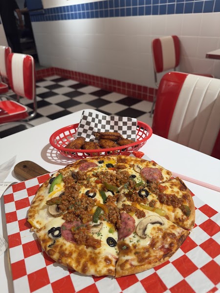 A pizza and a basket of chicken wings served on a red and white checkered paper in a diner-style restaurant.