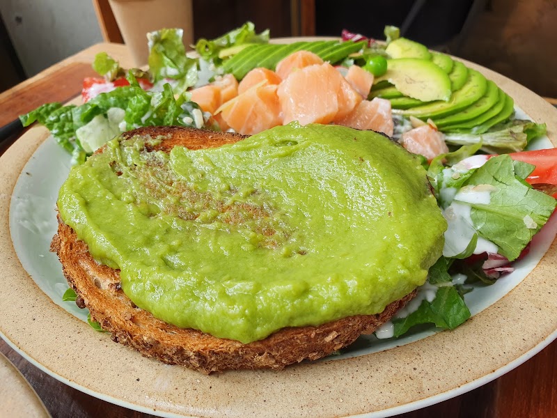 Avocado toast with salmon and fresh salad on a ceramic plate.