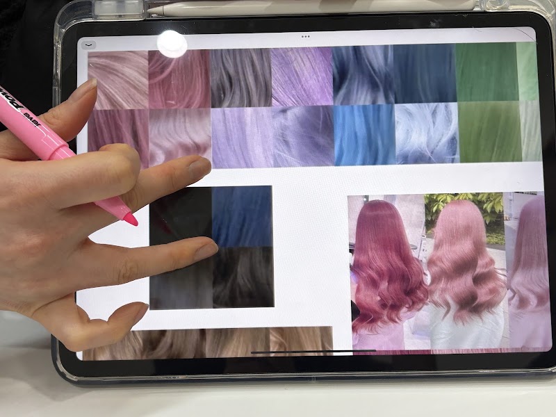A person using a pink highlighter on a tablet screen showing a grid of hair color samples and photos of dyed hair