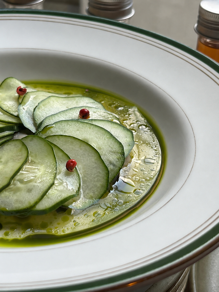 Thinly sliced circular cucumbers arranged with bright green herb oil and red peppercorns