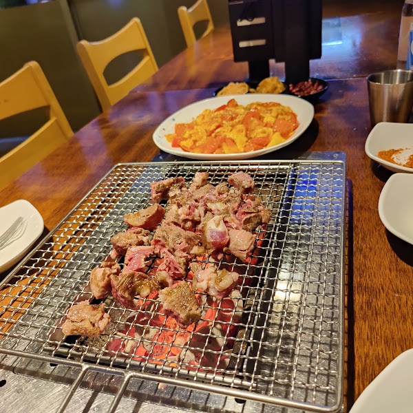Meat grilling over hot coals with tomato and egg stir-fry side dish