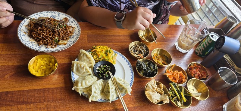 Black bean noodle jjajangmyeon plate with steamed dumplings and side dish bowls