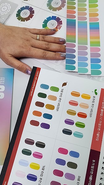 A person's hand with metallic nail polish rests on a desk with color theory charts and nail color palettes.