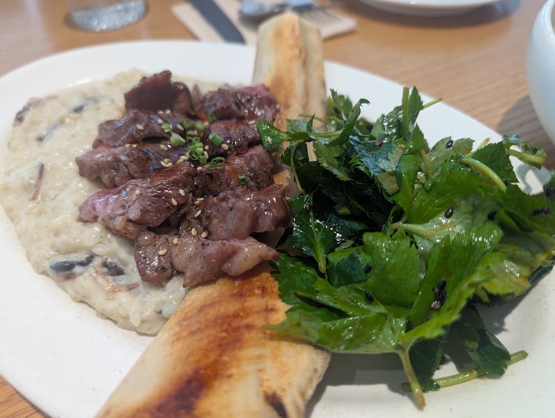 Grilled steak slices over creamy mushroom risotto with fresh greens and flatbread