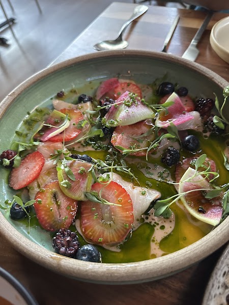 Colorful fish crudo topped with sliced strawberries, melon radishes and berries