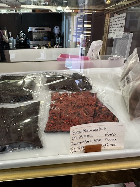 A glass display counter in a chocolate shop showing various bark chocolates with handwritten labels