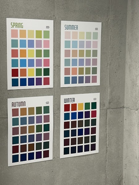 Four seasonal color palette posters hanging on a gray concrete wall in a personal color consultation studio.