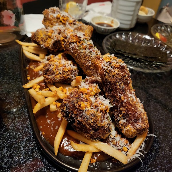 A platter of breaded fried ribs topped with shredded cheese and crunchy bits, served with french fries in a dark brown sauce.