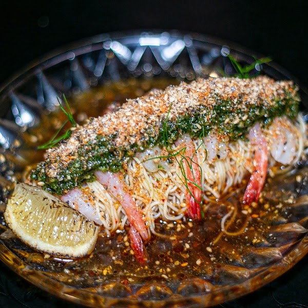 A gourmet cold noodle dish topped with shrimp, herbs, and breadcrumbs, served on a patterned glass plate.