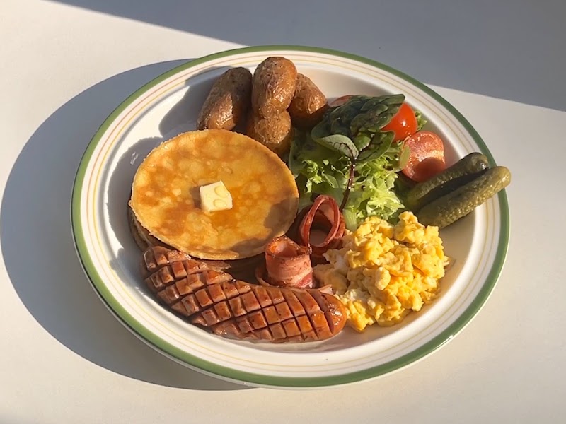 Hearty brunch plate with golden pancake, butter, scrambled eggs, grilled sausage, roasted potatoes, and fresh salad greens