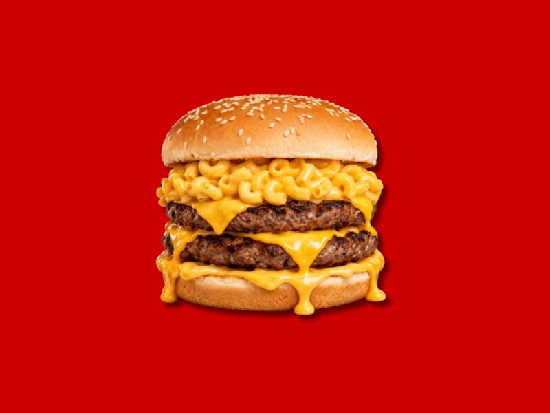 A double cheeseburger topped with macaroni and cheese on a solid red background.