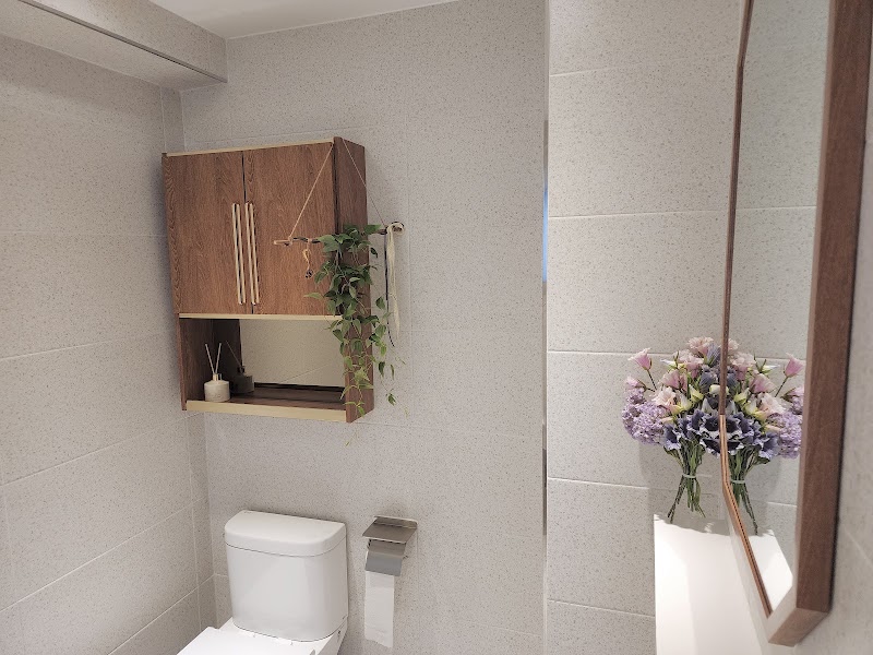A modern, clean bathroom with light grey speckled tiles, a wood-framed mirror, and a wall-mounted wooden cabinet with a plant