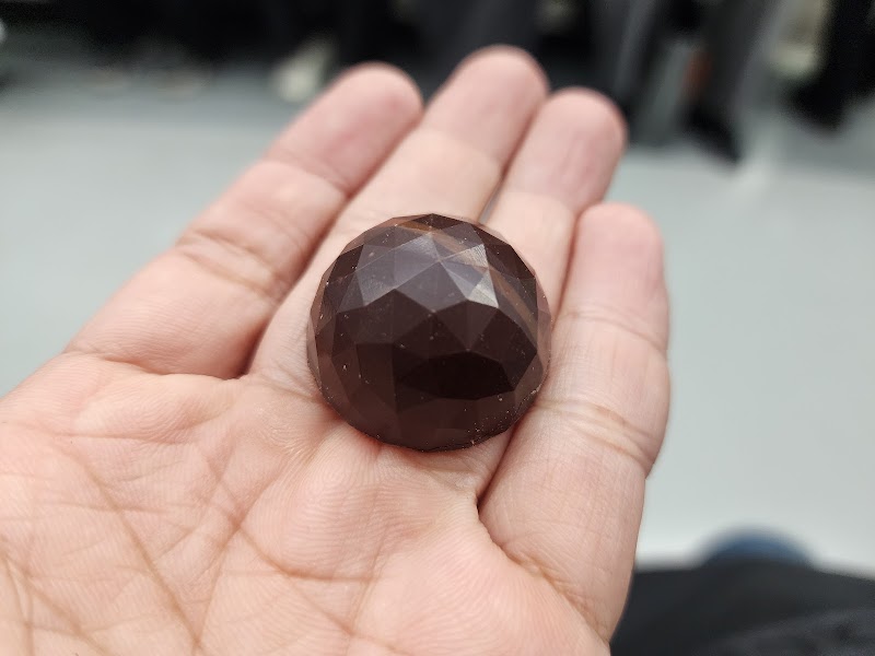 A faceted dark chocolate truffle held in the palm of a hand showcasing geometric details