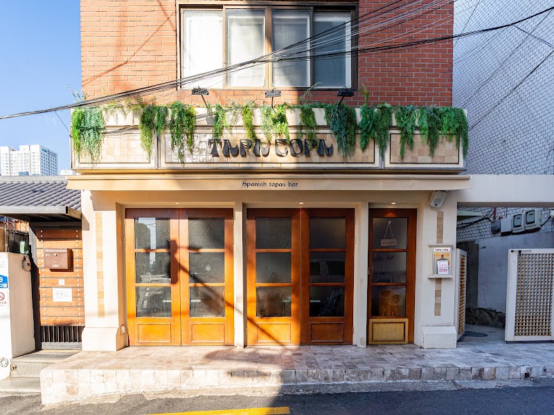 Exterior entrance of Tapa Copa with wooden paneled doors and lush hanging ivy