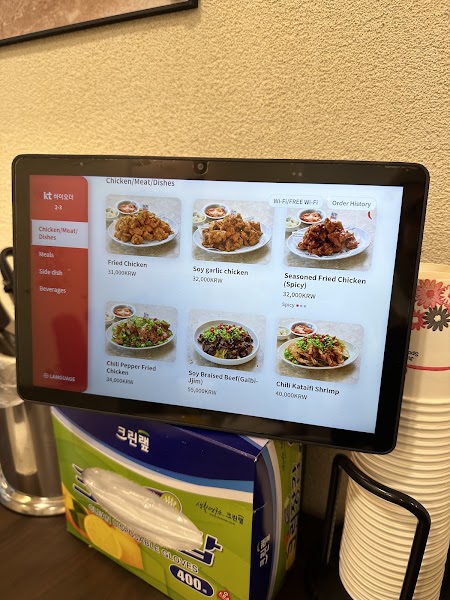A tablet at a restaurant table displaying a digital menu with pictures of chicken, beef, and shrimp dishes.