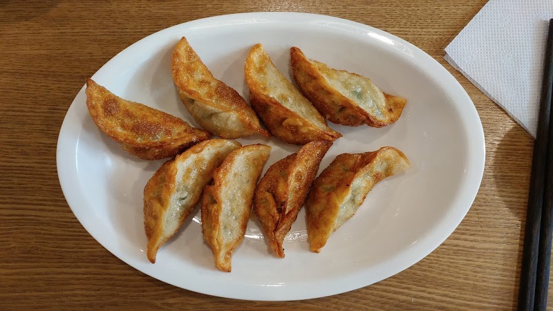A plate of eight golden-brown fried dumplings served on a white oval dish on a wooden table.