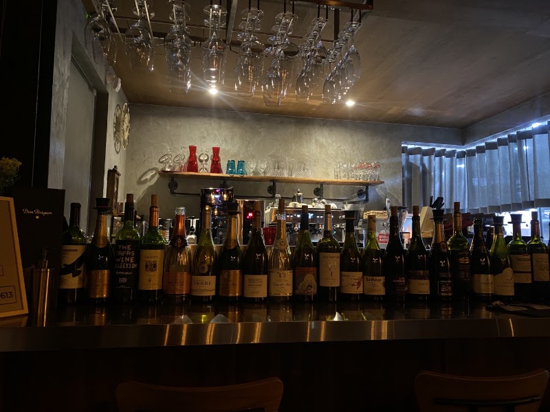 Row of wine bottles on a metal bar counter with hanging glassware at Bistro oven and vine in Seoul.