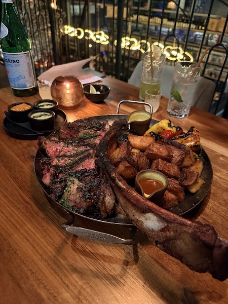 Grand scale Tomahawk steak platter with seared potatoes on dark wood table