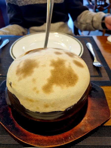 A round, domed bread-covered pot served on a wooden platter at Saffron restaurant table
