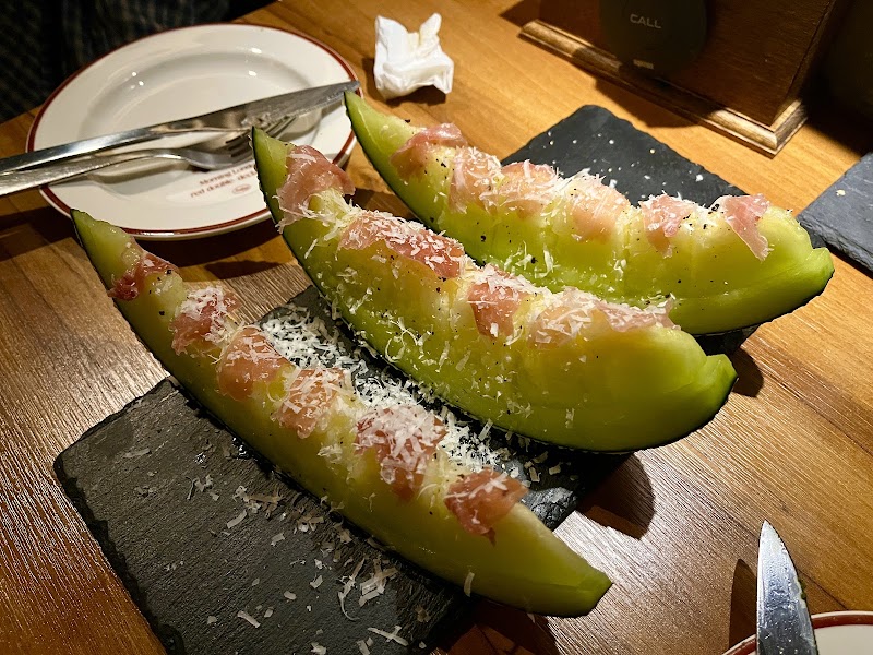 Melon slices topped with cured ham and shaved cheese on dark slate