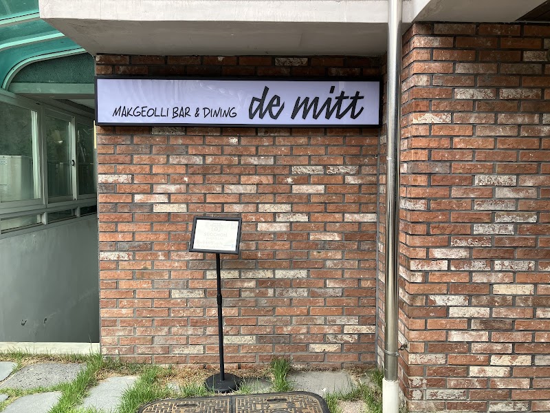 Red brick exterior wall of de mitt with illuminated makgeolli bar and dining signage